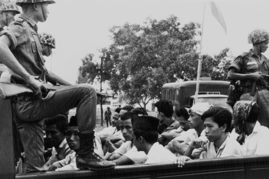 A soldier points a weapons at young men in the back of a truck