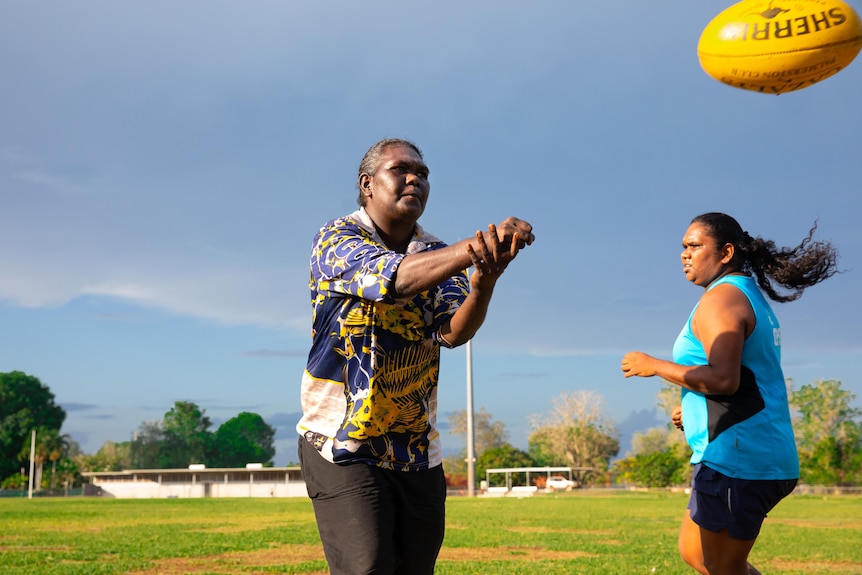 An older woman handballs a yellow football to someone out of view