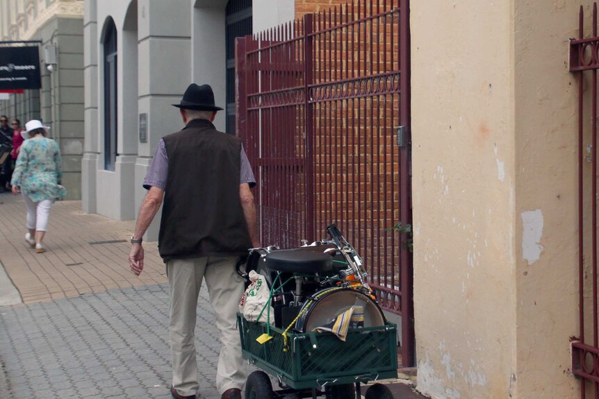 Hubert Davies walks to a gig in Fremantle, wheeling his drum gear in a green trolley behind him.