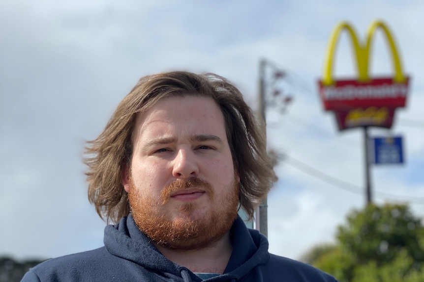 A man standing with a McDonald's fast food restaurant sign behind him.