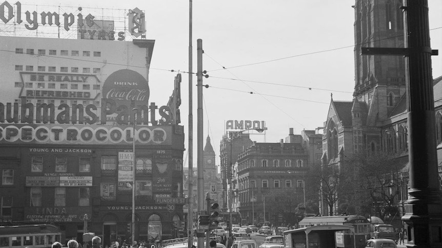 Black and white photo of busy city street corner with neon advertising signs.