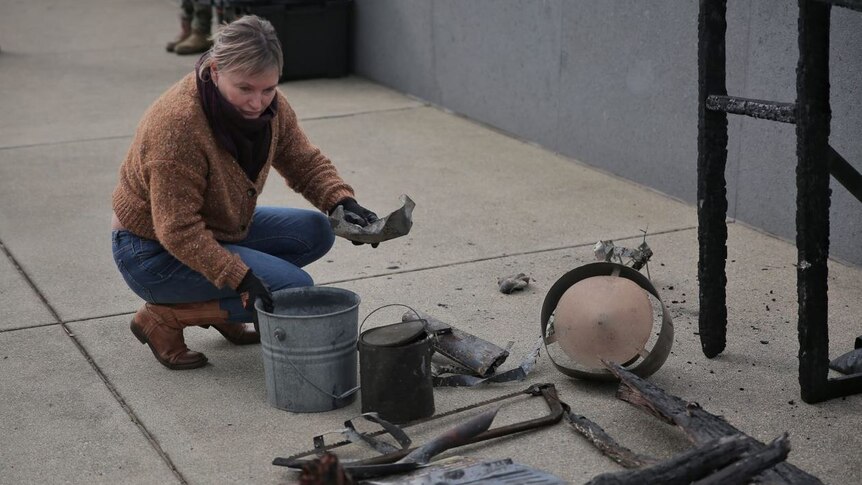 Melinda Plesman squatting down, putting pieces of burnt building materials on the paved ground.