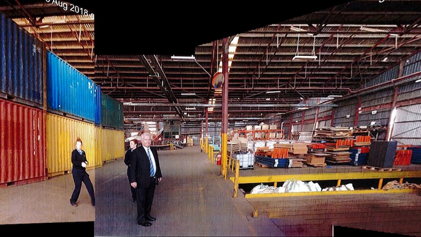 A man in a suit and two women in a fairly empty warehouse.