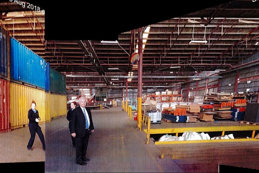 A man in a suit and two women in a fairly empty warehouse.