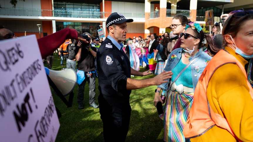 Police speak to a woman at a Maylands protest for and against drag queen story time.