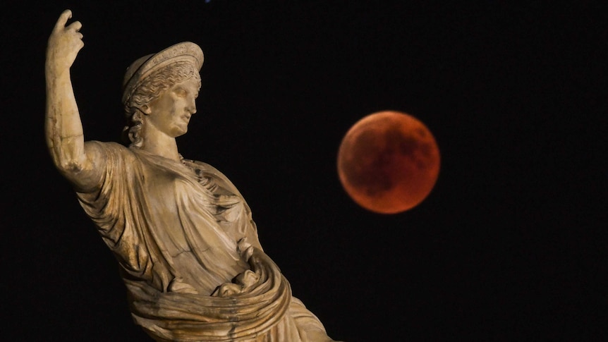A statue of ancient Greek goddess Hera in the foreground with a red full moon in the background.