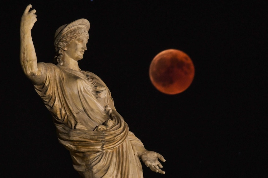 A statue of ancient Greek goddess Hera in the foreground with a red full moon in the background.