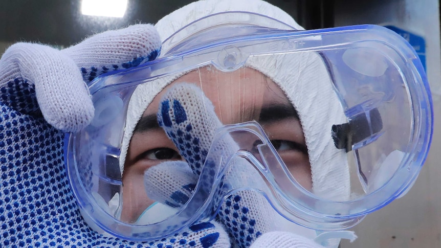 A person uses their gloved finger to clean the inside of clear goggles.