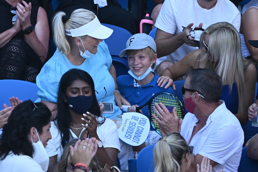 A young tennis spectator holds a racquet given to him by Nick Kyrgios.