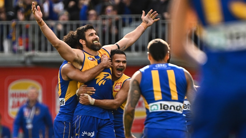 Josh Kennedy holds his arms in the air as West Coast players surround and hug him