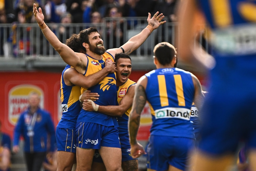 Josh Kennedy holds his arms in the air as West Coast players surround and hug him