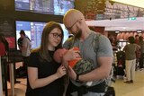 Belma and Demir Cancar hold baby Zeid in front of a departure sign at an airport