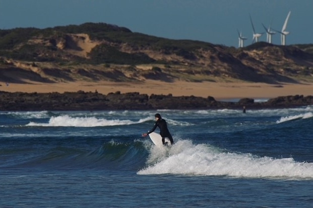 A surfer in a dark wetsuit shreds up a wave in front of a headland.