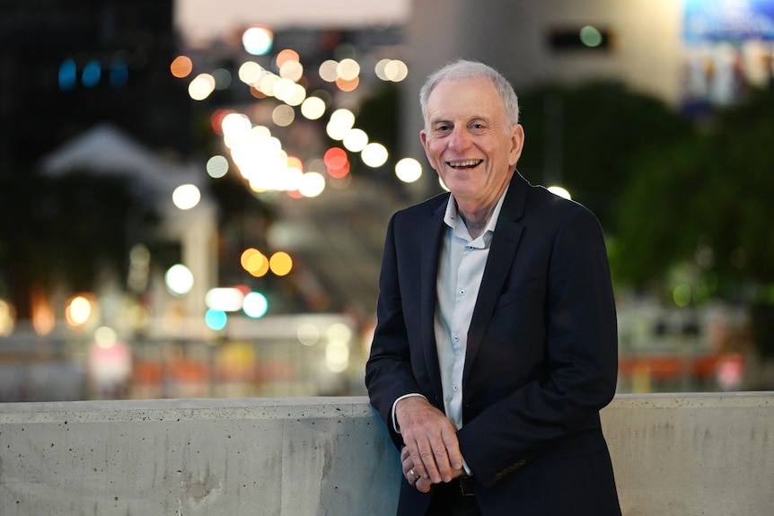 Professor Robert Henry stands in a suit smiling on a bridge with city lights in the distance