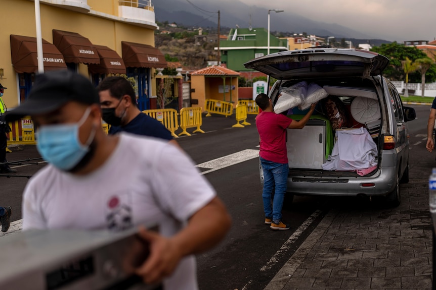 People wearing masks pack boxes into a white van. The sky above them is dark.