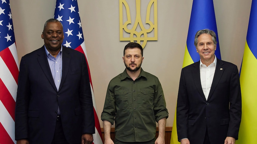 President Volodymyr Zelenskyy and two US envoys post in front of national flags.