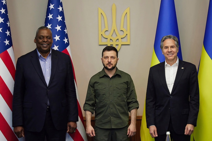 President Volodymyr Zelenskyy and two US envoys post in front of national flags.