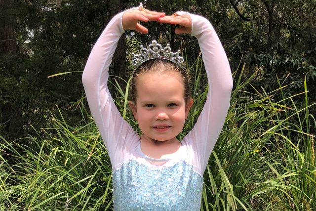 Alice Salisbury stands smiling in a blue tutu, striking a pose. 