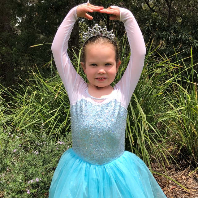 Alice Salisbury stands smiling in a blue tutu, striking a pose. 