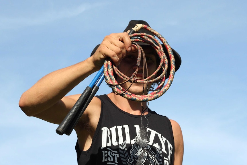 A man holds up a red and white whip.