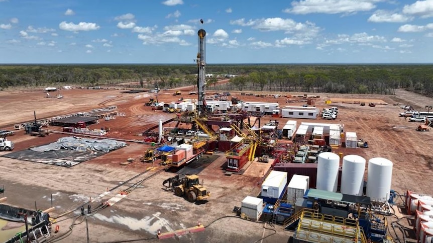 A gas exploration well in the desert, surrounded by a drill rig and equipment.