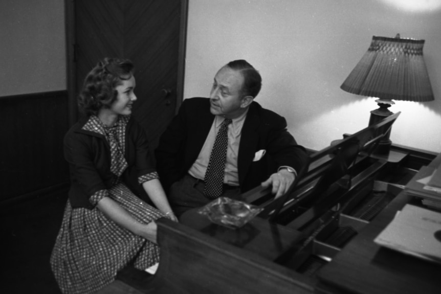 A black and white photo of debbie reynolds and arthur freed sitting at a piano. 