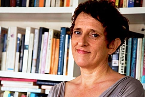 Upper body view of Charlotte Wood standing in front of shelves lined with books.