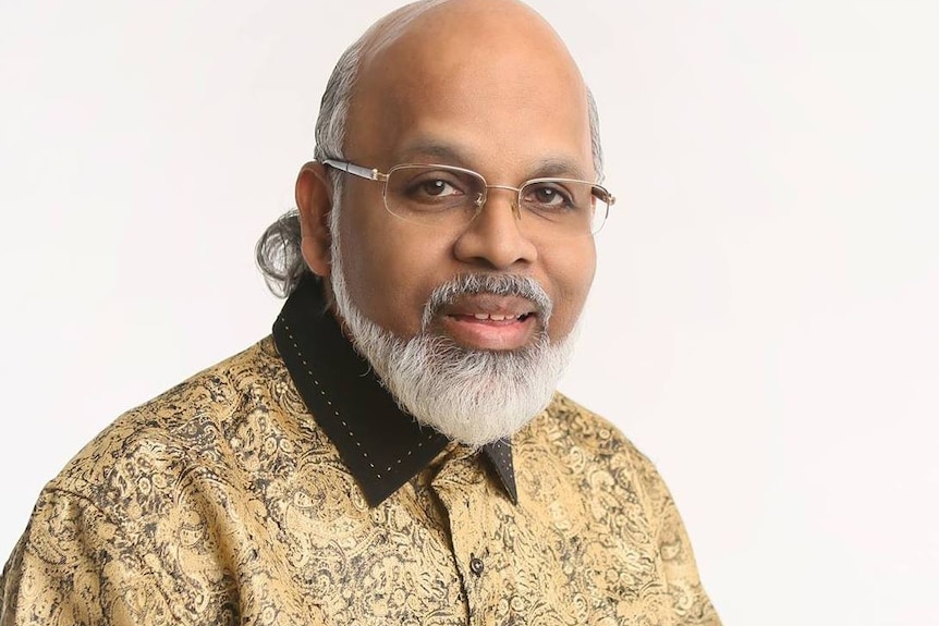 A man with a silver beard, wearing glasses and a gold and black shirt.