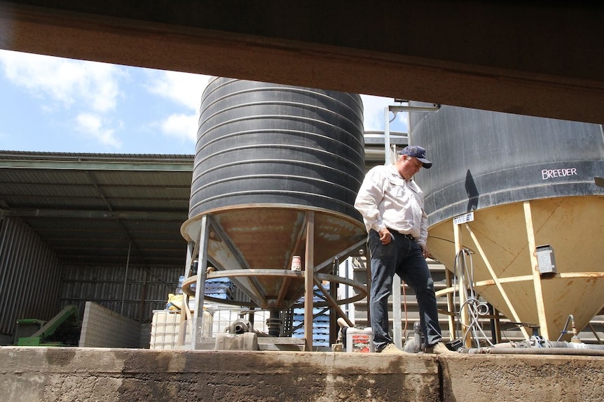 Tony Newman stands next to a shed and a storage tank.