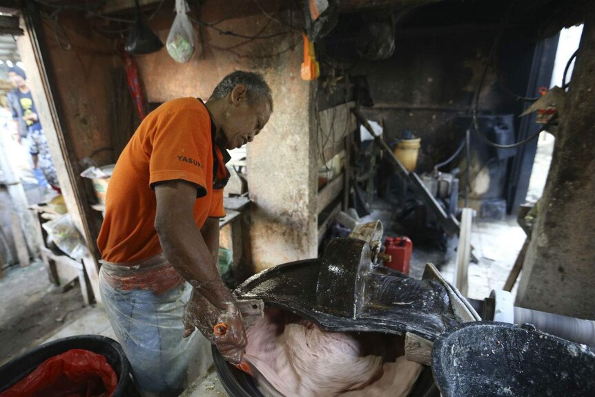 A man processes a pinkened beef mix with his hands in a mixer at an Indonesian market stall.