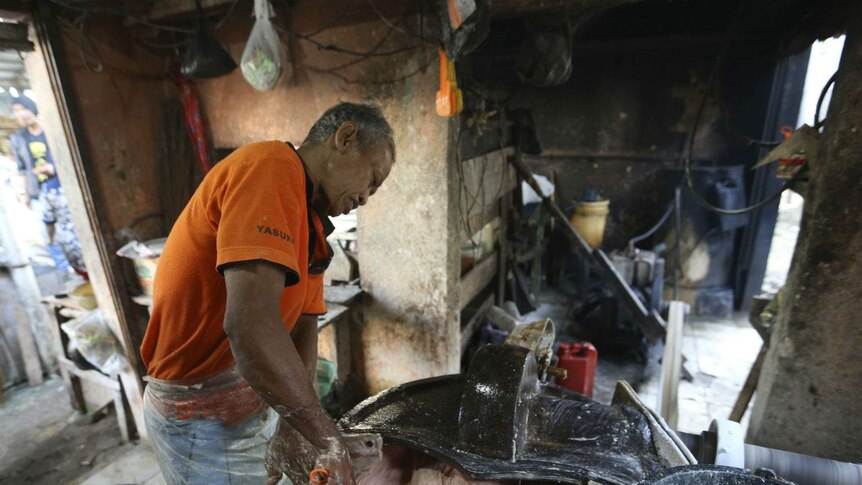 A man processes a pinkened beef mix with his hands in a mixer at an Indonesian market stall.