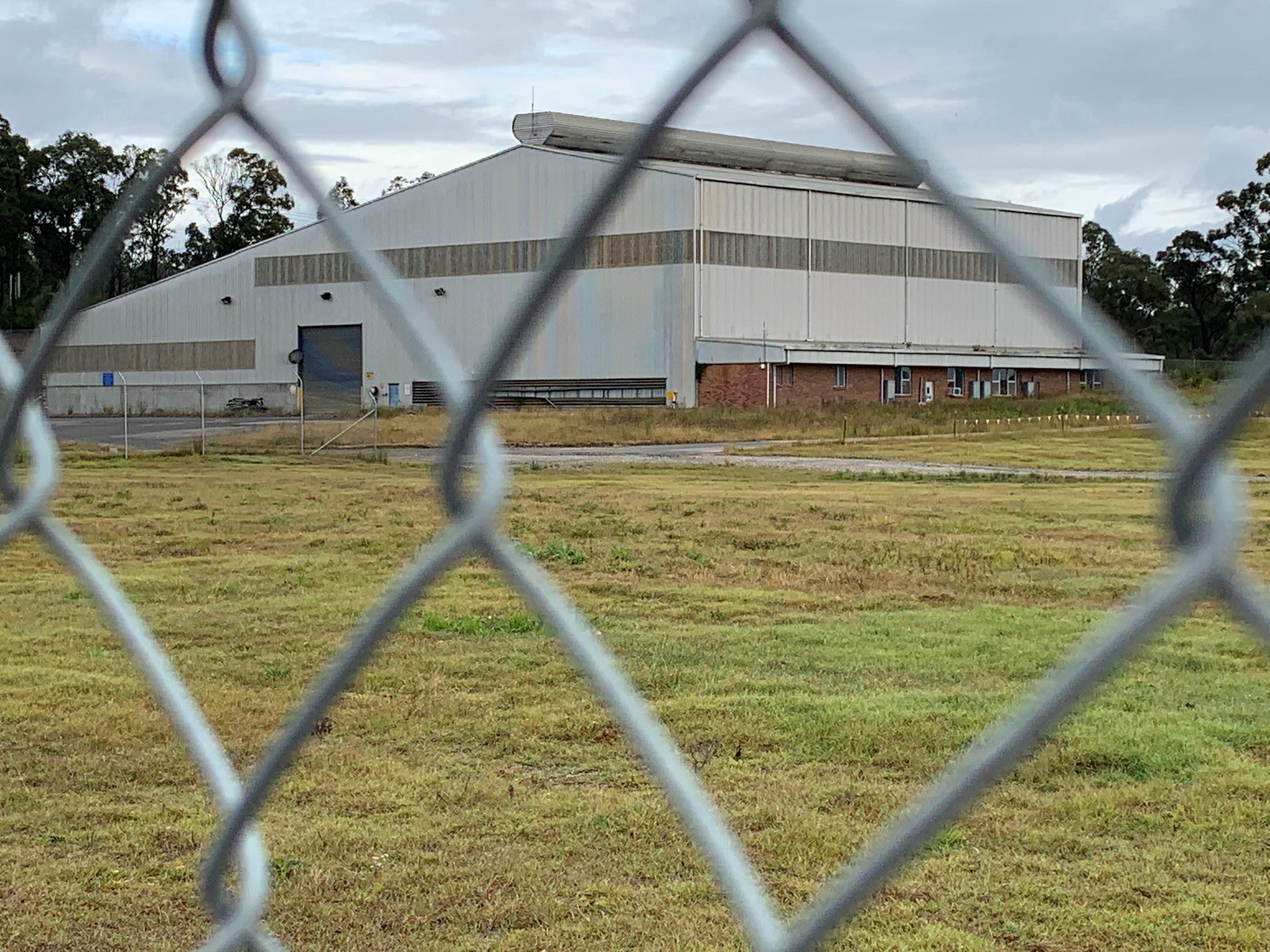 A close up of a chain link fence, with a grassy field and shed in the distance.