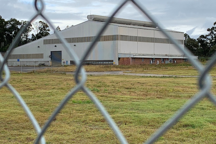 A close up of a chain link fence, with a grassy field and shed in the distance.