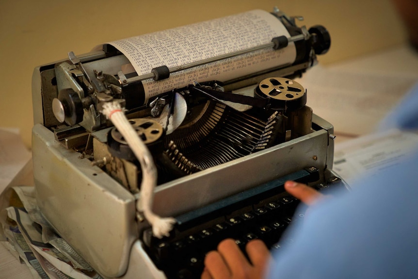 Close view of a person's hands on a chunky typewriter with paper covered in text