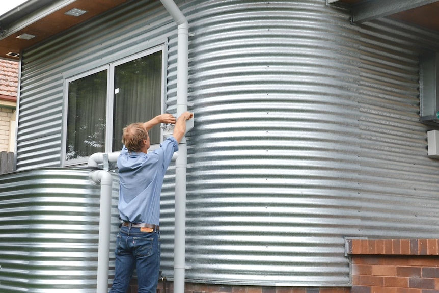 Andy Lemann cleans leaves from the drain outside his renovated house, which is clad in silver corrugated iron.