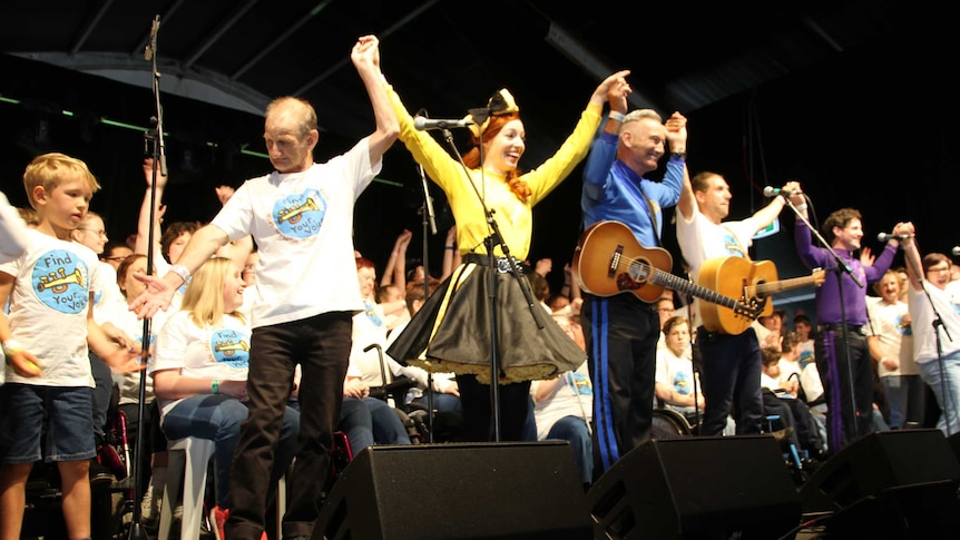 A large group of people hold hands on stage, preparing to take a bow.