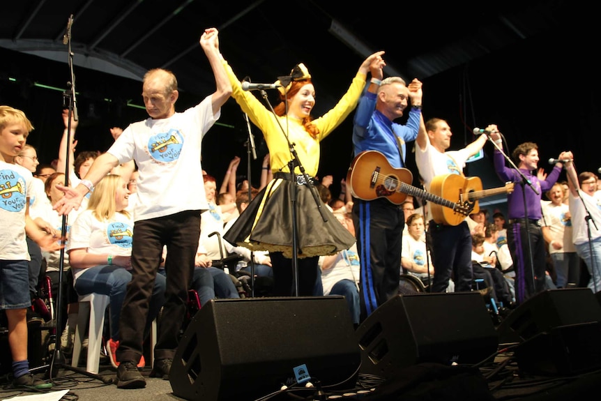 A large group of people hold hands on stage, preparing to take a bow.