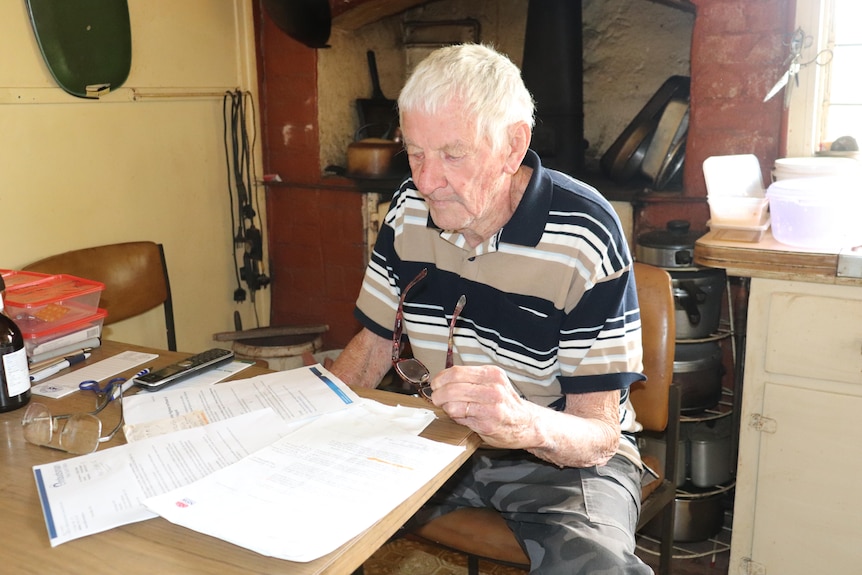 An elderly man sits at his kitchen table looking at several documents sent to him from Transport for NSW