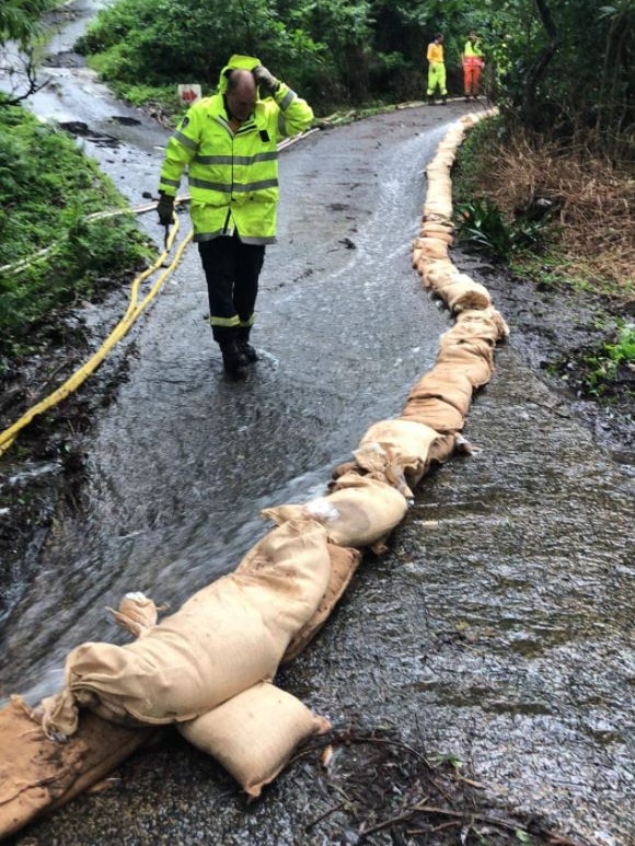 Man in high vis walks past sand bags and water 
