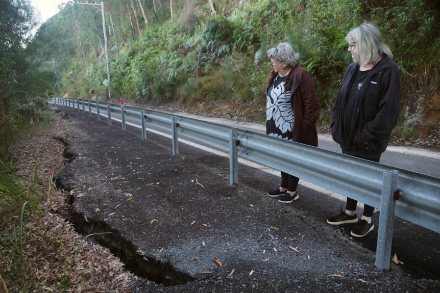 Two women look at huge crack in the road