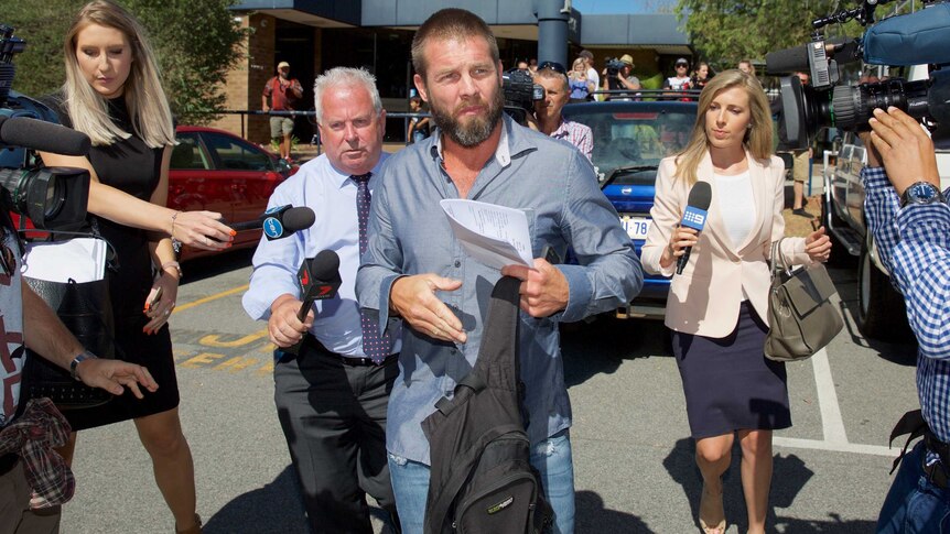 Ben Cousins walks away from Armadale Magistrates Court holding a backpack and piece of paper with journalists trailing behind.