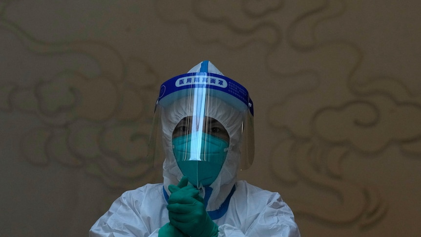 A worker sits wearing full protective equipment to take COVID test samples