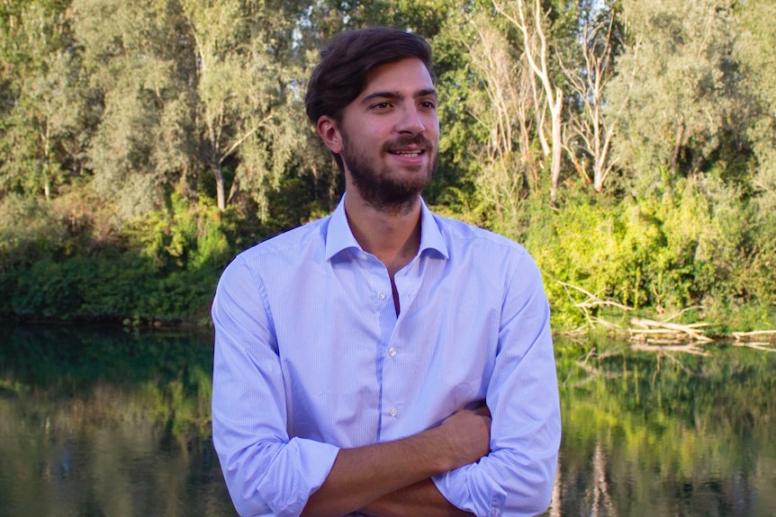 A man in a white shirt stands with his arms folded