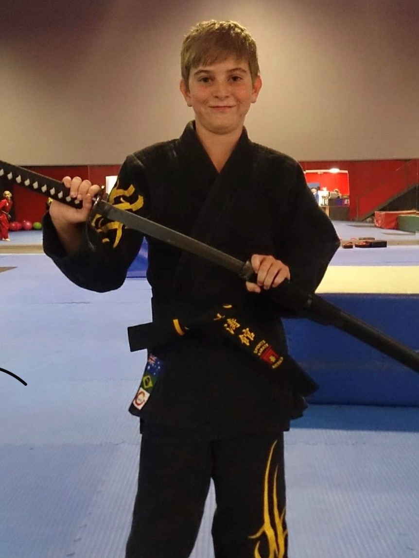 Young boy with black karate uniform holding a samurai sword