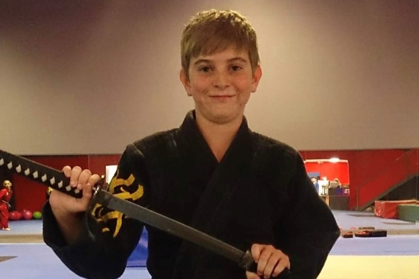 Young boy with black karate uniform holding a samurai sword