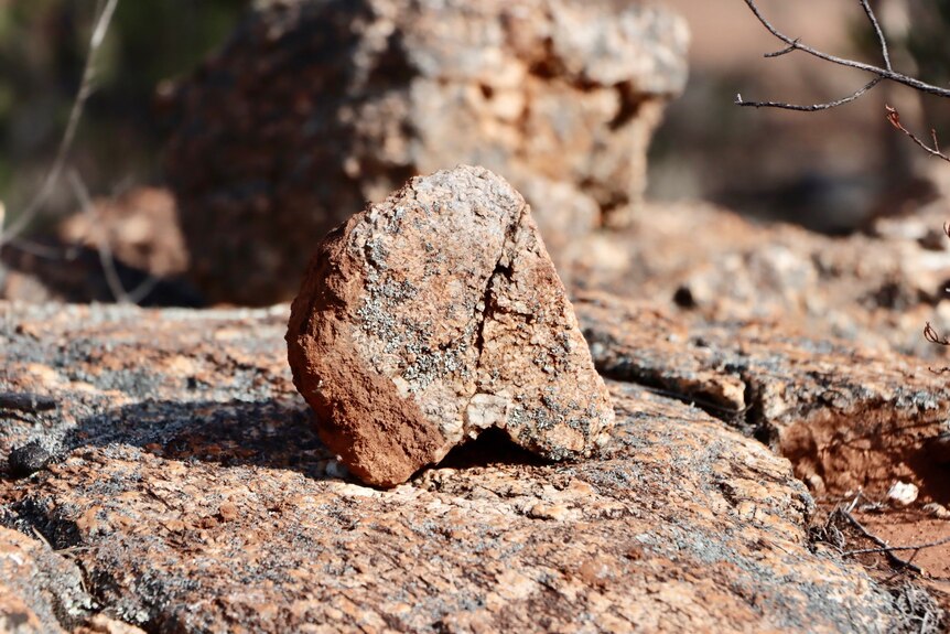 A reddish rock sits on a larger, similar rock.