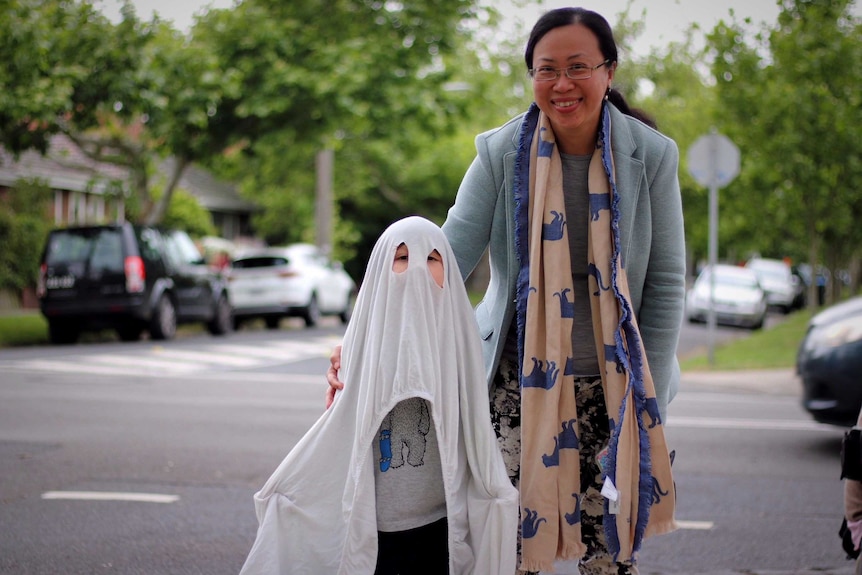 A young boy dresses up as a ghost in Melbourne for Halloween with his mum.