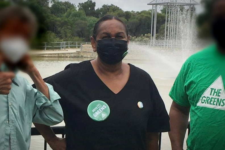 A woman wearing a mask stands amongst a group of people in front of a fountain