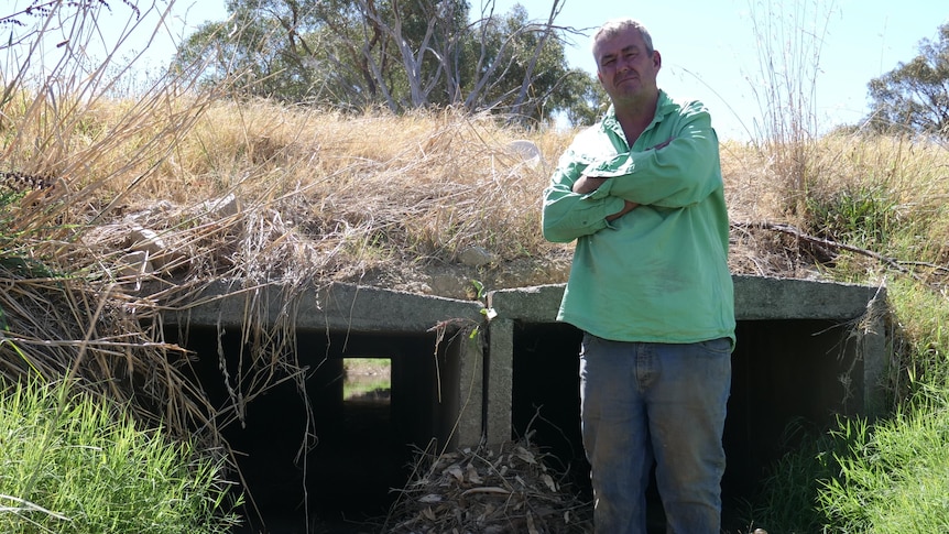 Man wearing green shirt stands in front of culvert.