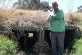 Man wearing green shirt stands in front of culvert.